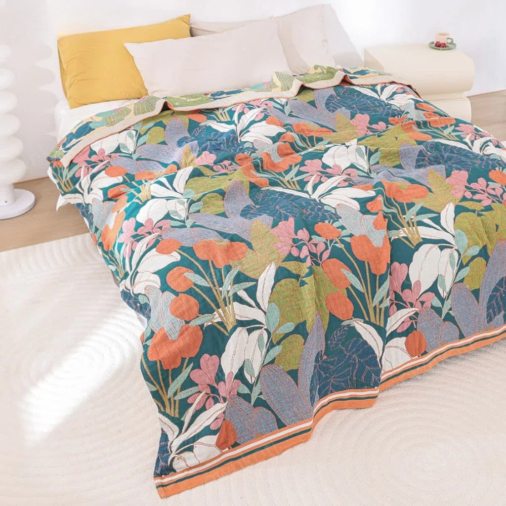 A cotton gauze blanket with a vibrant floral and leaf pattern in shades of teal, orange, pink, and white.