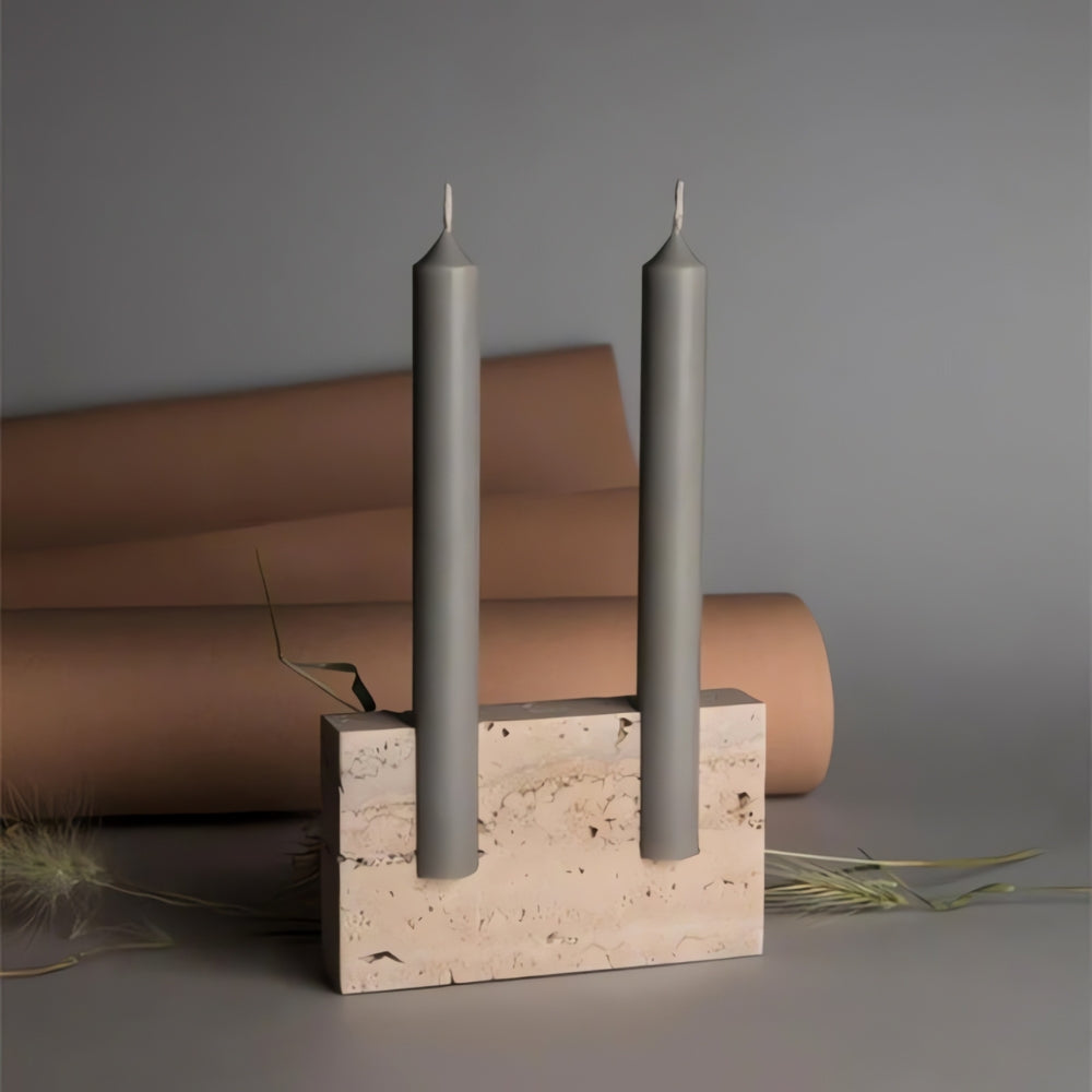 Dual taper candle holder made of beige travertine stone with two grey taper candles.