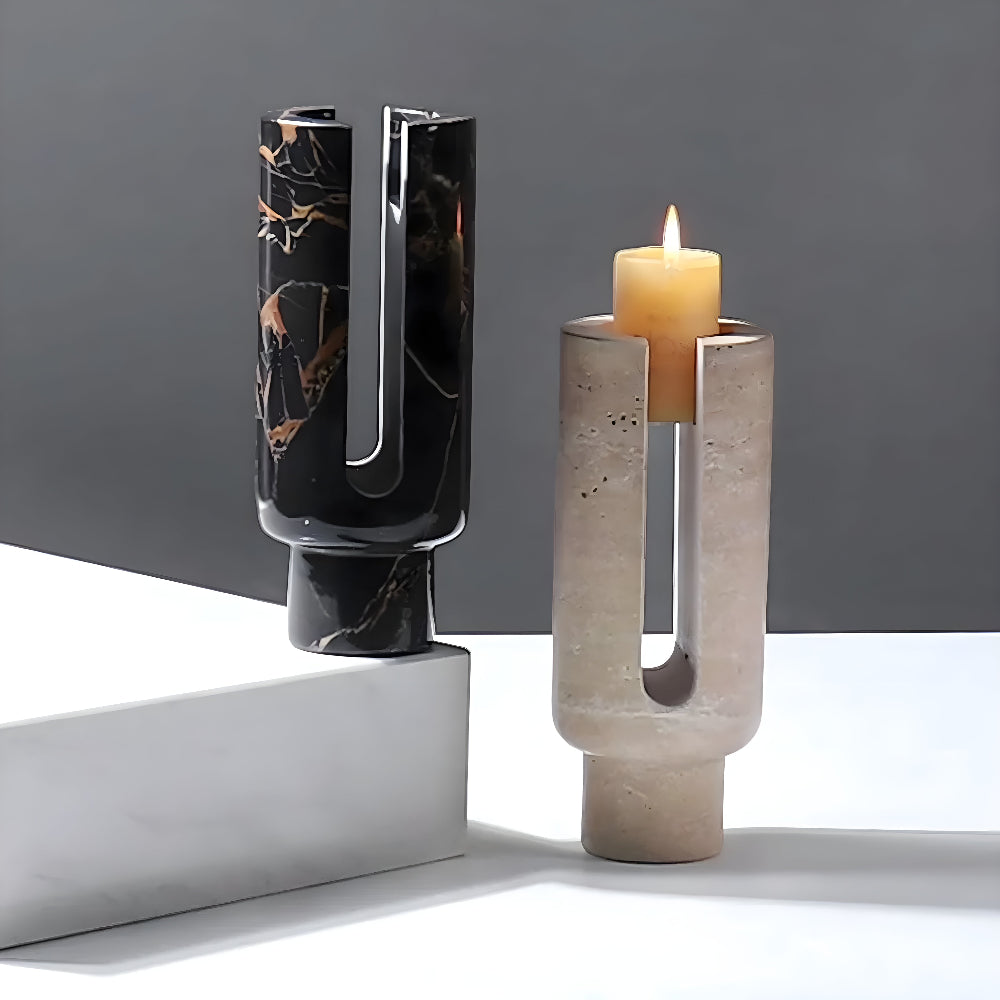 Two sculptural candle holders, one black marble and one beige stone, on a white surface.