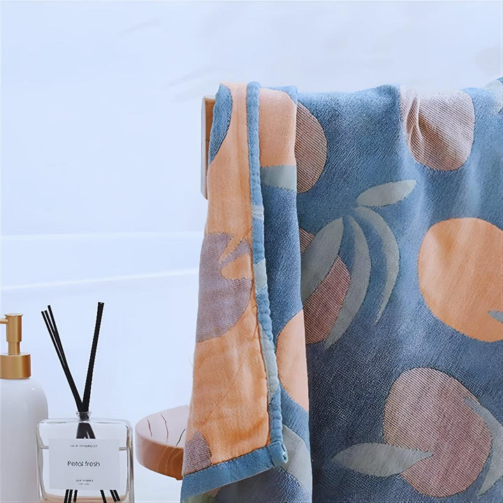 Blue cotton beach towel with an orange and green fruit pattern, draped over a wooden rack.