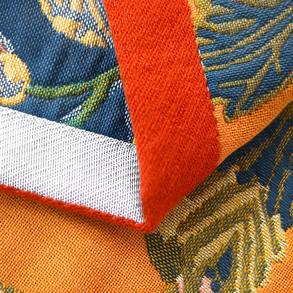 Close-up of a reversible cotton bath towel with orange trim and a blue and orange hibiscus pattern.