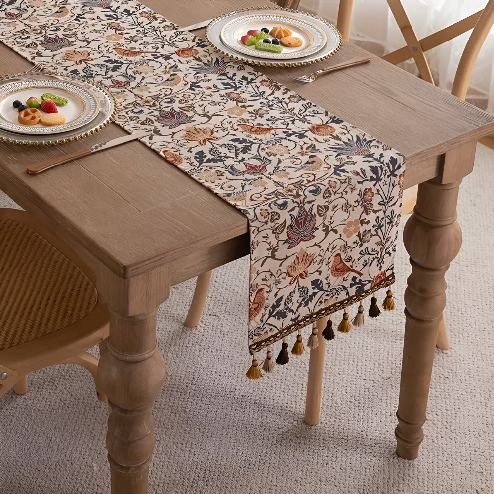 Vintage floral and bird jacquard table runner with tassels on a wooden table.