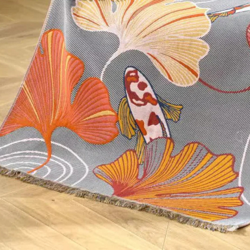 Cotton gauze towel with a koi fish and ginkgo leaf pattern in orange, yellow, and white on a grey background.