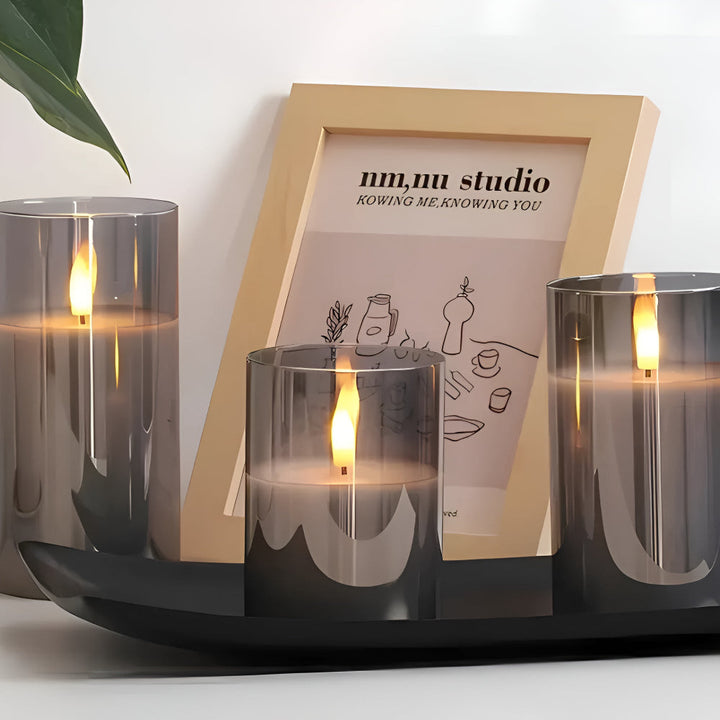 Three grey glass flameless candles with 3D LED flames on a black tray, next to a framed picture.