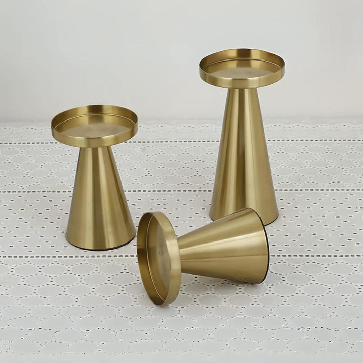 Set of three artisan brass candle holders in varying sizes on a white lace tablecloth.