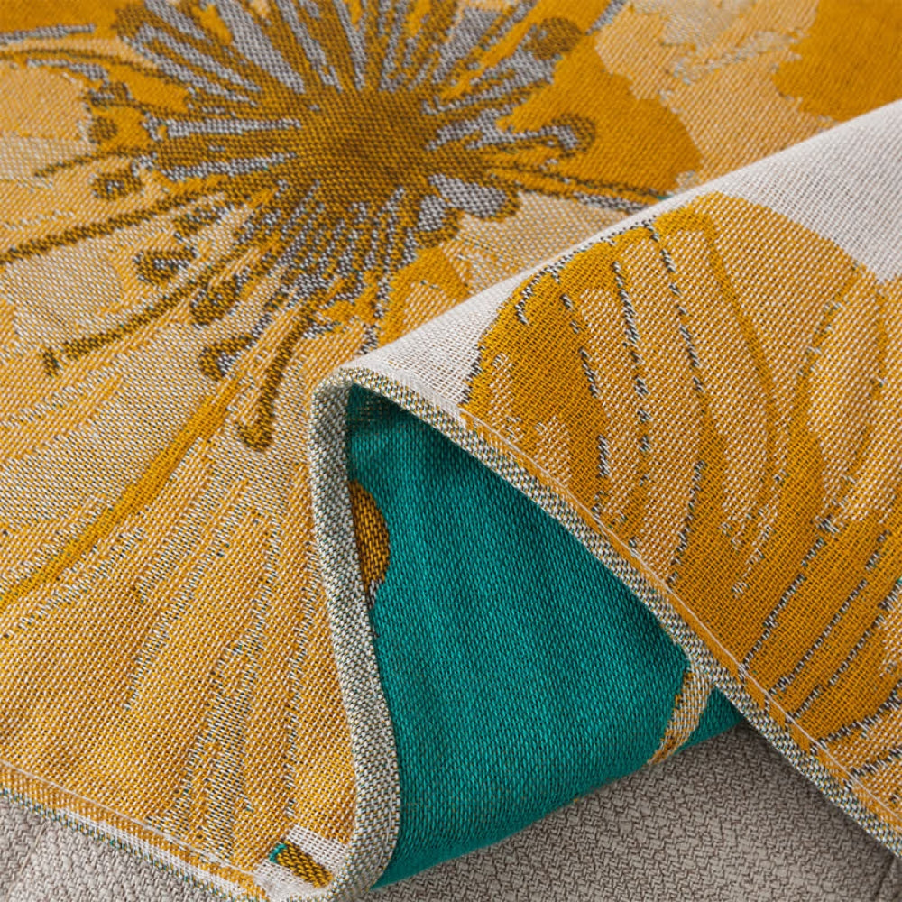 A close-up of a yellow and teal floral patterned cotton bath towel, folded to show both sides.