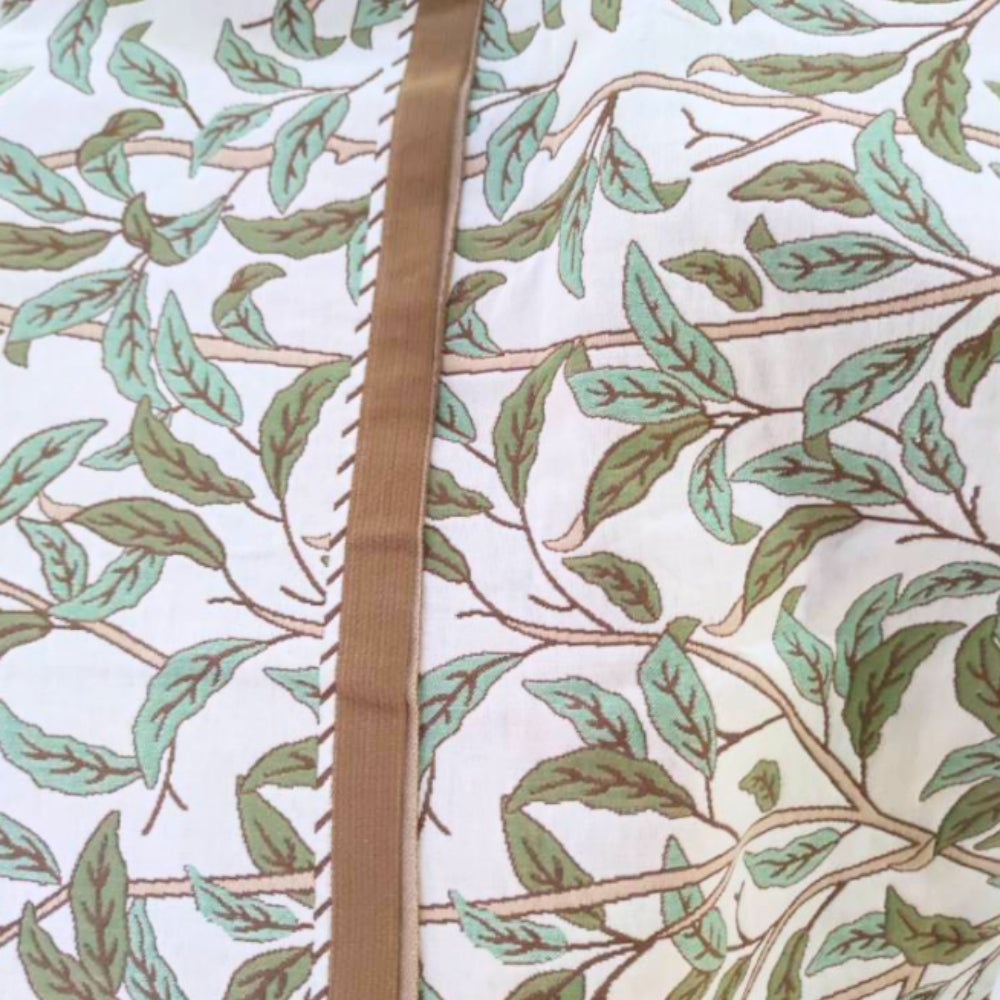 White cotton bath towel with a repeating pattern of green leaves and brown branches, and a vertical brown ribbon detail.