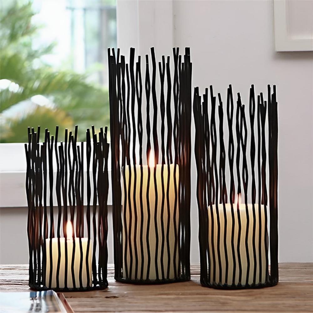Three black iron desk candle holders with geometric designs, each holding a lit candle.