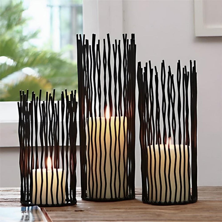 Three black iron desk candle holders with geometric designs, each holding a lit candle.