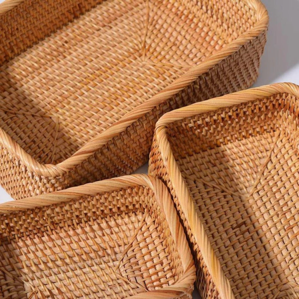 Three rectangular rattan storage baskets with woven texture and braided edges.