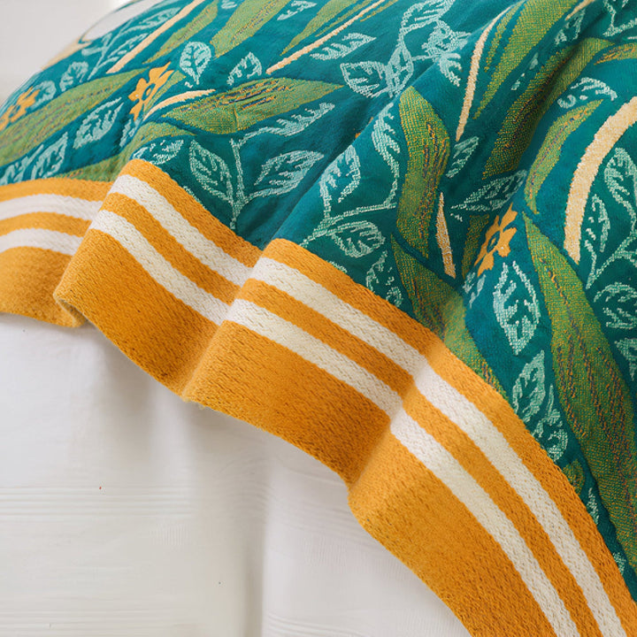 Green botanical bloom cotton blanket with yellow and white striped border.