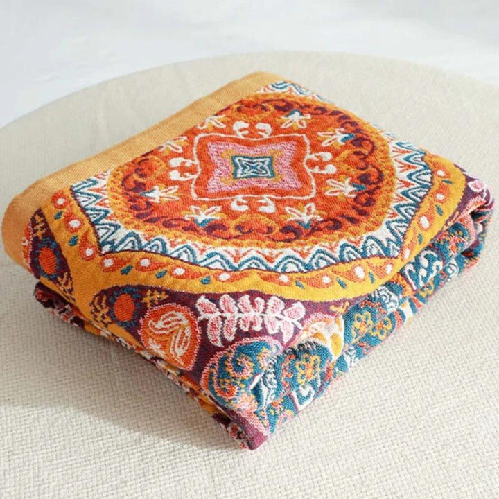 Folded cotton bath towel with a colorful boho geometric and floral pattern in orange, yellow, blue, and purple.