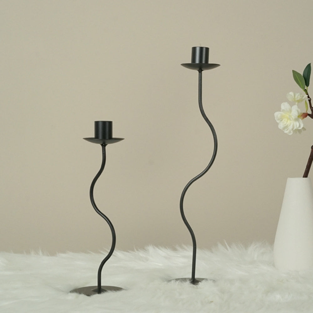 Two black wavy iron candle holders on a white fluffy surface.