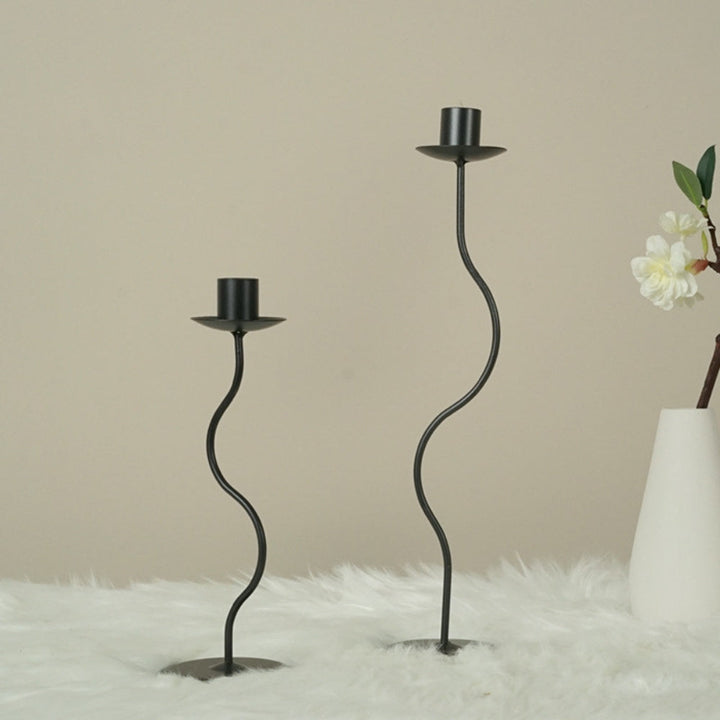 Two black wavy iron candle holders on a white fluffy surface.