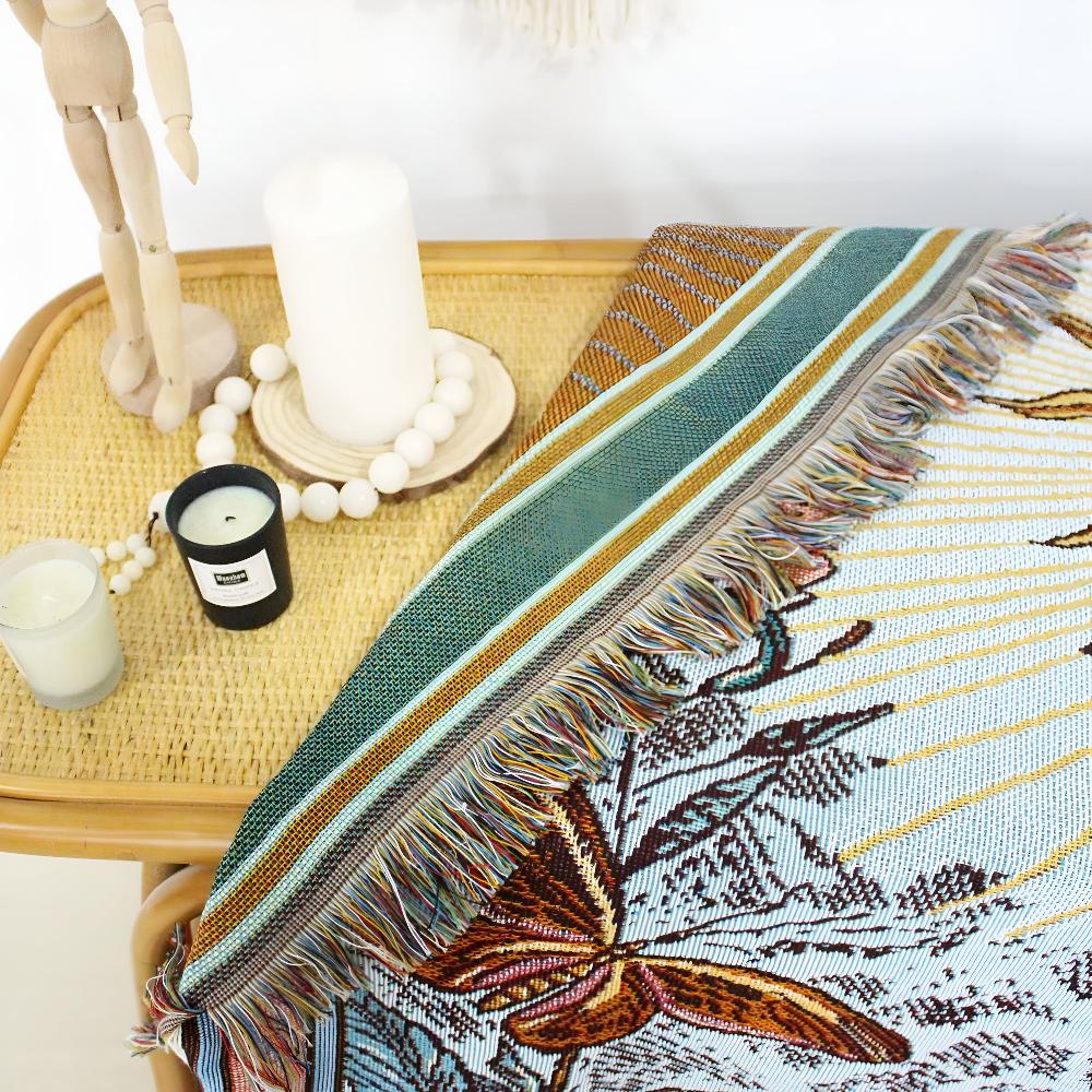 Woven tapestry throw with a celestial sun design and fringed edges, draped over a rattan tray with candles.