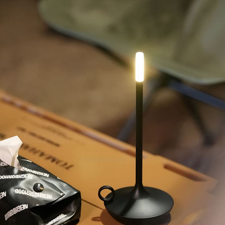 Black portable table lamp with a bright LED light on top, placed on a wooden table.