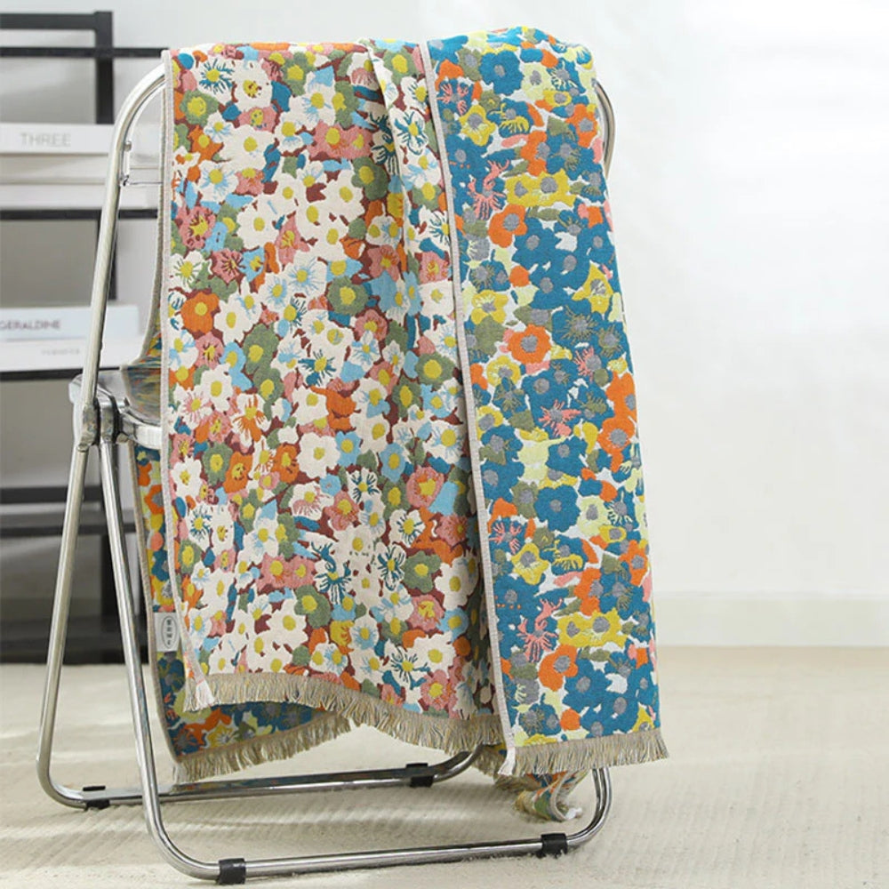 Two reversible cotton bath towels with colorful floral prints draped over a metal chair.