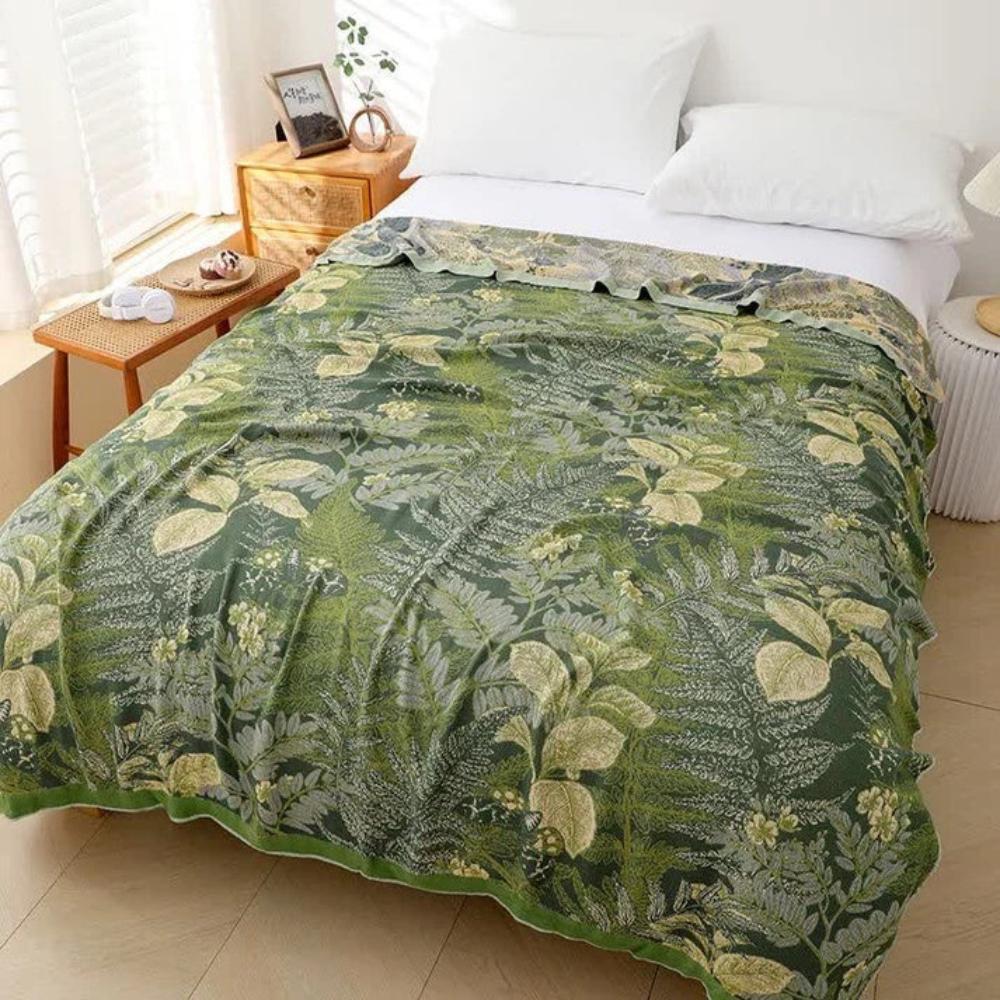 Bamboo fiber cooling quilt with a green leaf pattern, draped on a bed with white pillows.