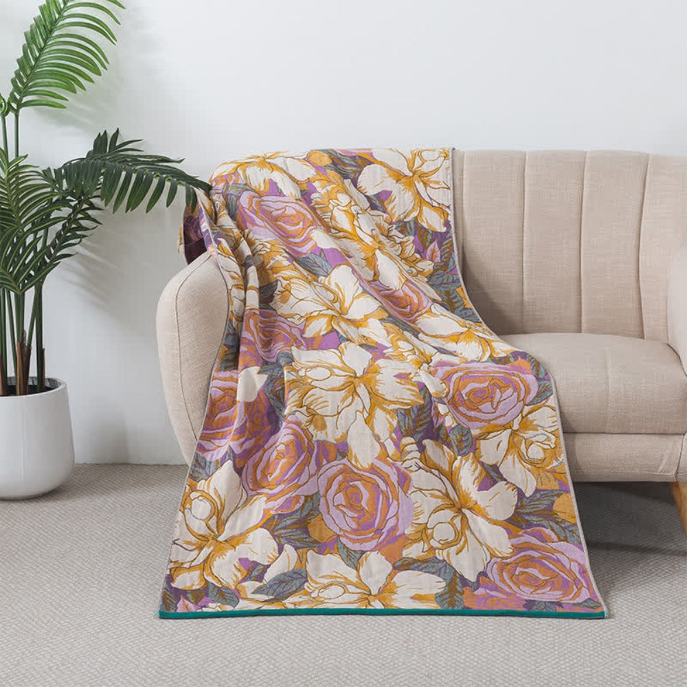 A throw blanket with a vintage rose floral design in purple and orange draped over a cream sofa.