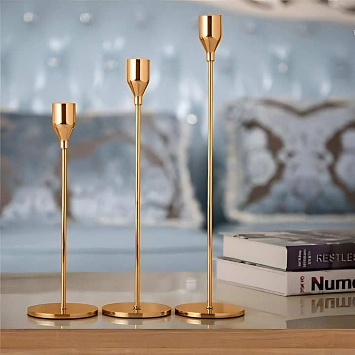 Set of three tall, gold stainless steel candle holders of varying heights on a reflective surface.