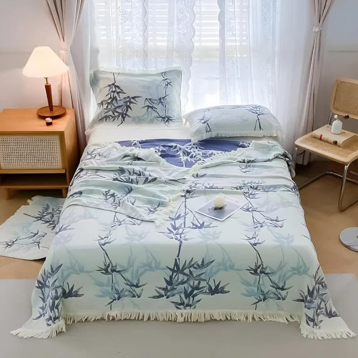 Bamboo Cotton Reversible Jacquard Throw with a blue bamboo leaf pattern and fringe detail on a bed.