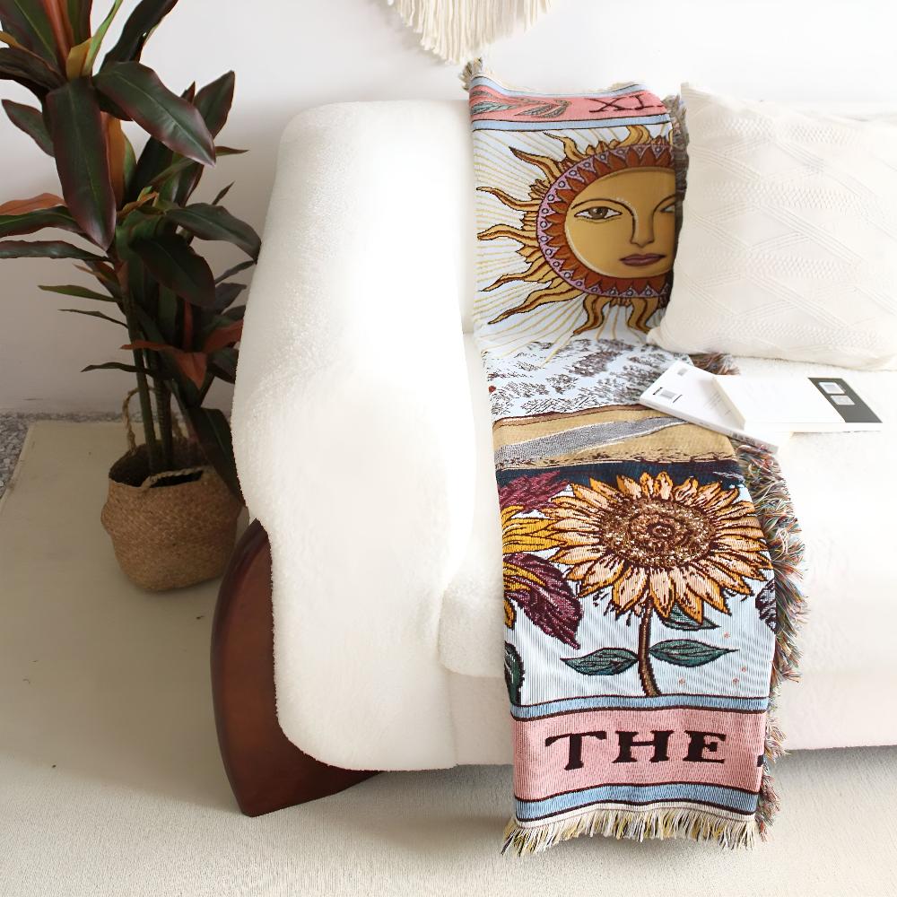 Boho style tapestry throw with a sun and sunflower design draped over a white couch.