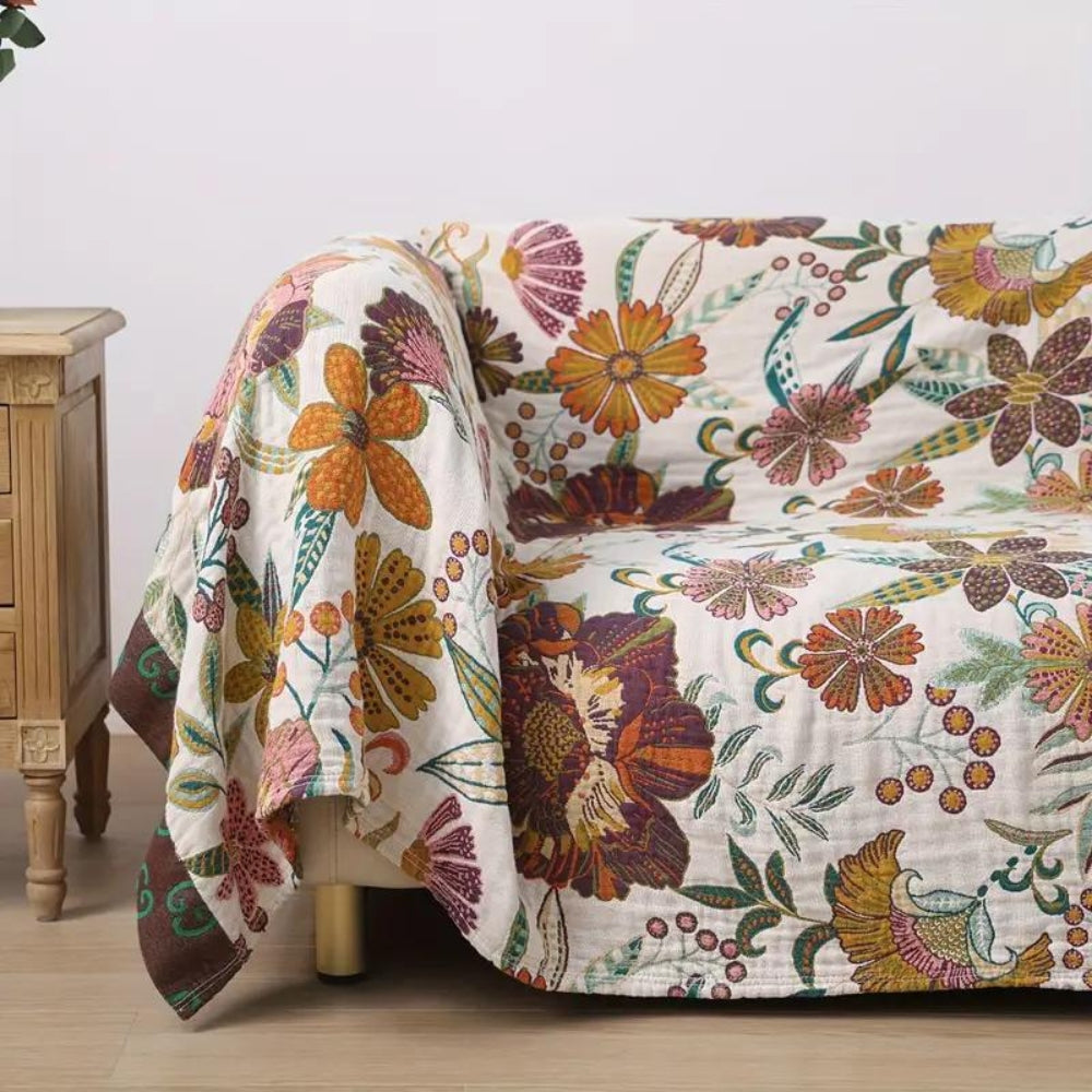A floral blanket throw with a white background and colorful flowers in shades of orange, purple, and pink draped over a sofa.