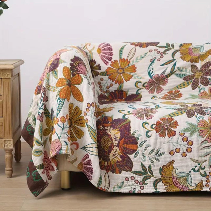 A floral blanket throw with a white background and colorful flowers in shades of orange, purple, and pink draped over a sofa.