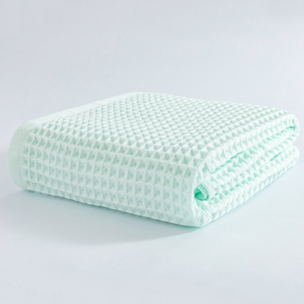 Light green cotton waffle weave bath towel folded on a white surface.