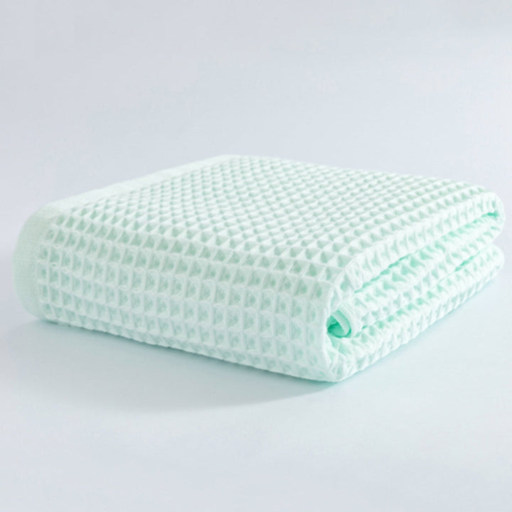 Light green cotton waffle weave bath towel folded on a white surface.