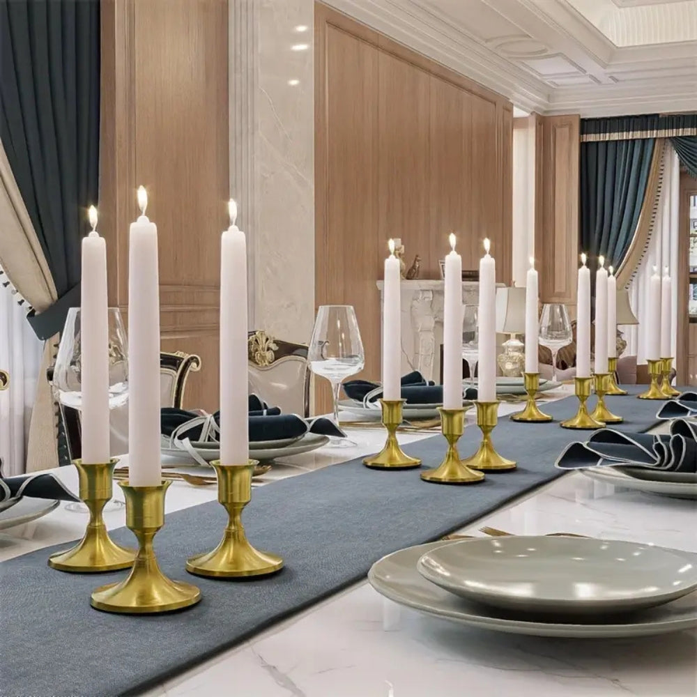 A long dining table set with white taper candles in gold vintage candle holders.