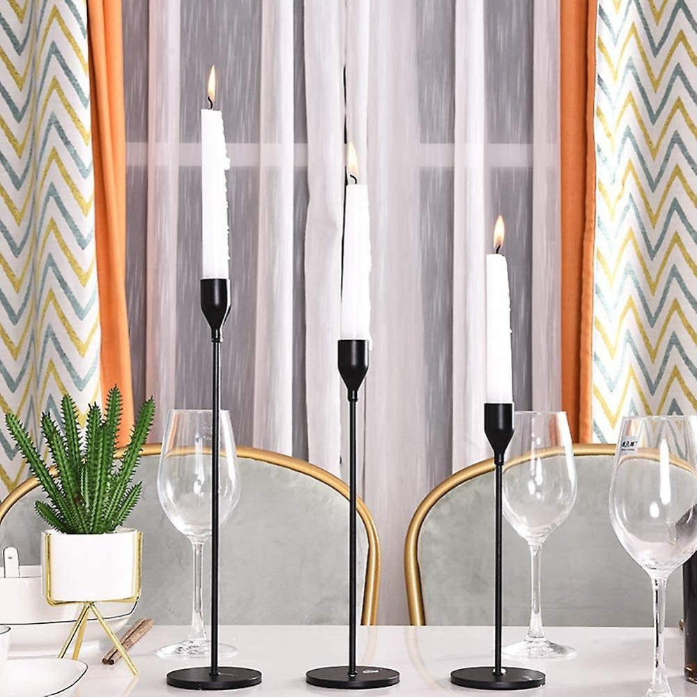 Set of three tall, modern stainless steel candle holders with white taper candles.