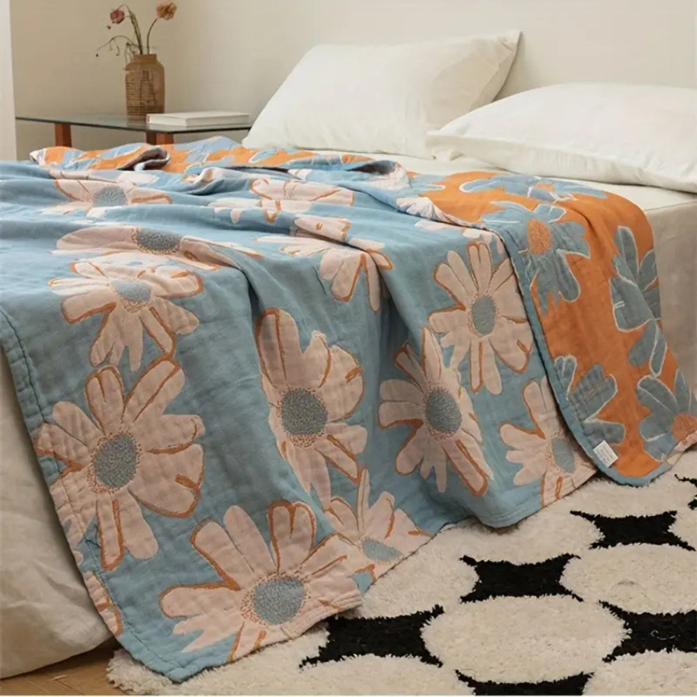 Blue cotton blanket with large pink and orange daisy pattern, draped on a bed with white pillows.