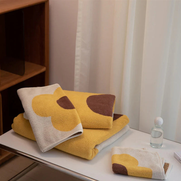 Yellow and brown floral cotton bath towels folded on a white surface.
