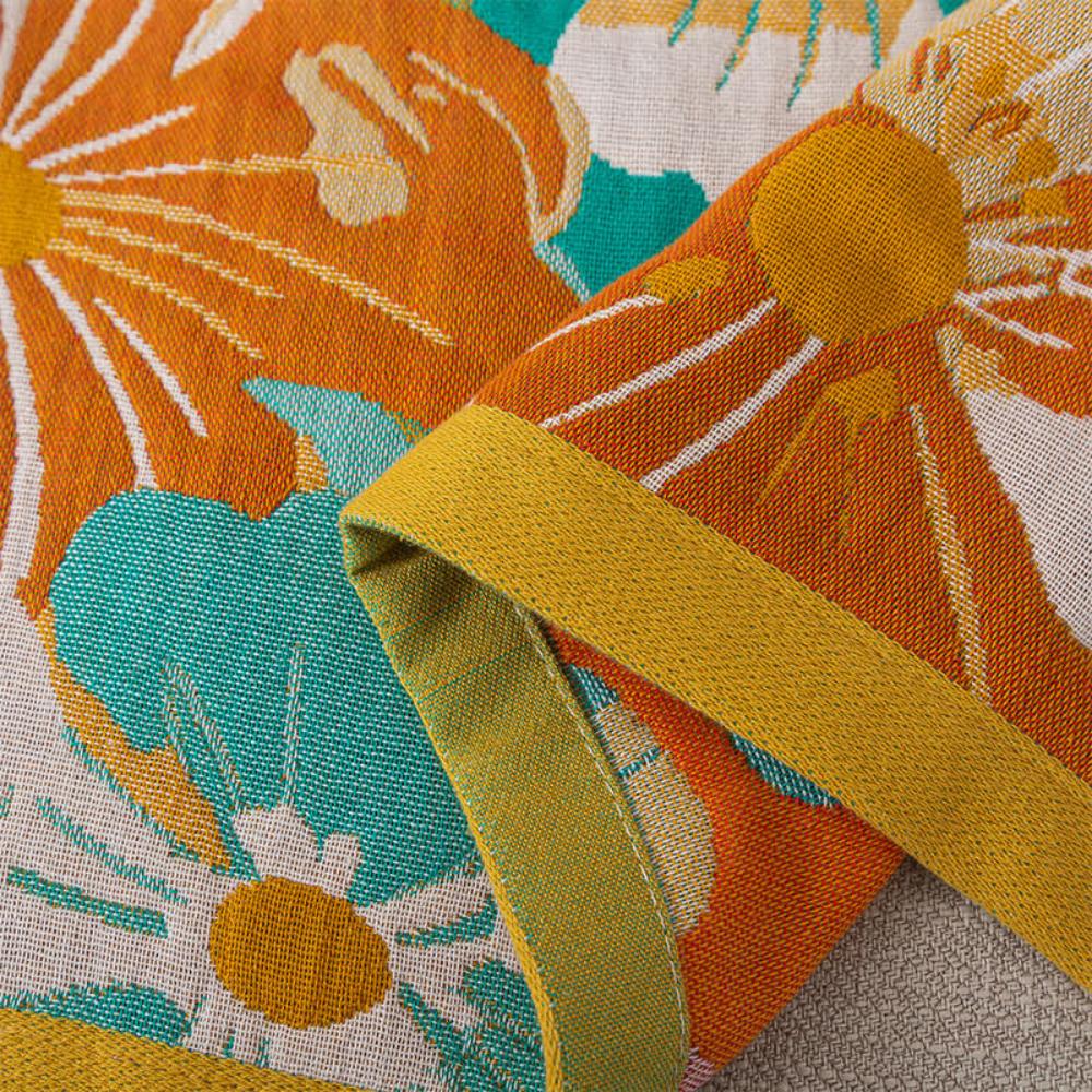 Cotton gauze bath towel with a bright orange and teal floral pattern and a mustard yellow trim.