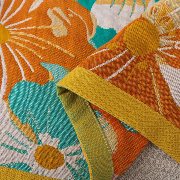 Cotton gauze bath towel with a bright orange and teal floral pattern and a mustard yellow trim.