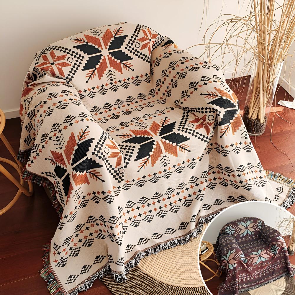 Cream-colored throw blanket with a geometric snowflake pattern in black and rust orange, draped over an armchair.