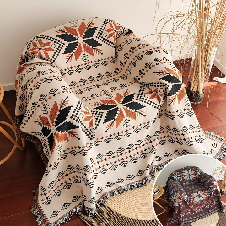 Cream-colored throw blanket with a geometric snowflake pattern in black and rust orange, draped over an armchair.