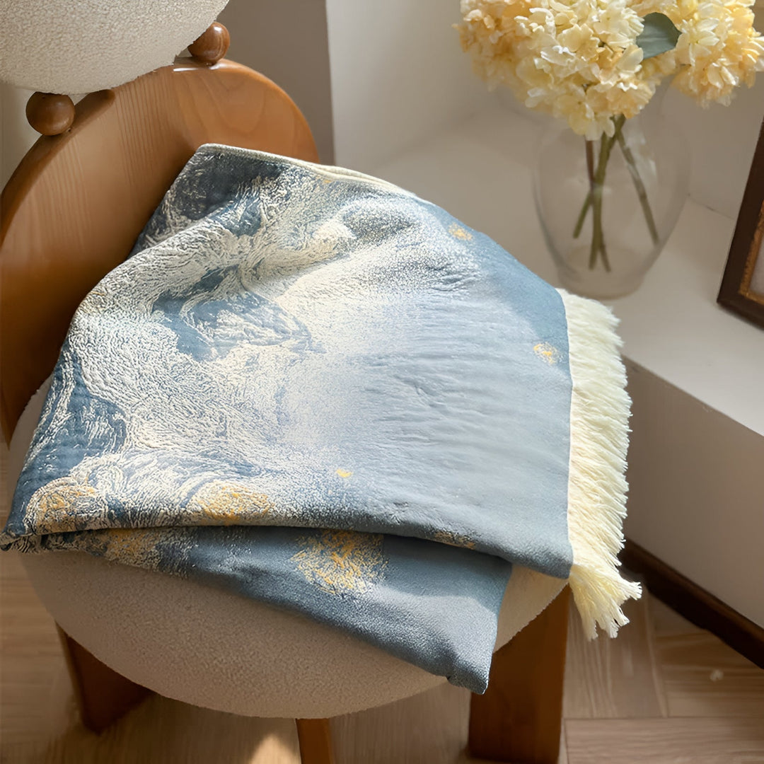 Blue and white patterned cotton towel with cream fringe draped over a chair.