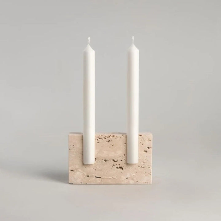 Travertine taper candle holder with two white candles on a light gray background.