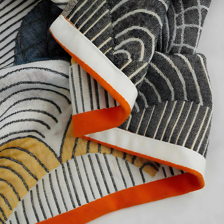 Close-up of a white cotton bath towel with a black and white wavy line pattern and orange trim.