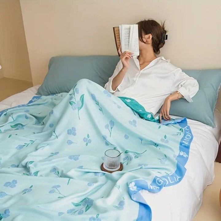 Woman reading in bed under a light blue blanket with a floral pattern and a blue border.