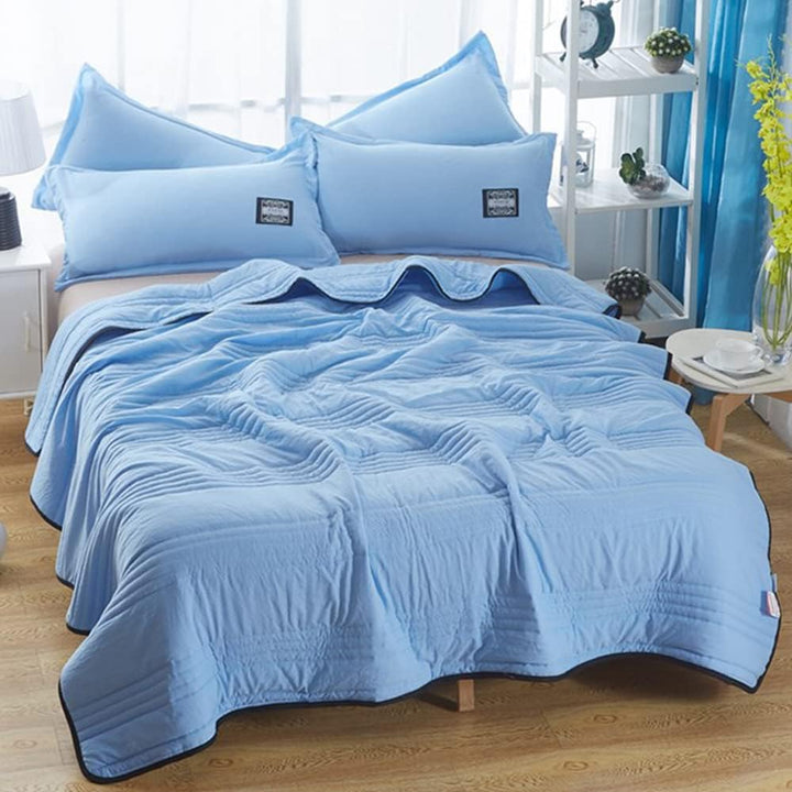 Light blue EverChill Ice Cooling Blanket draped on a bed with matching pillows.