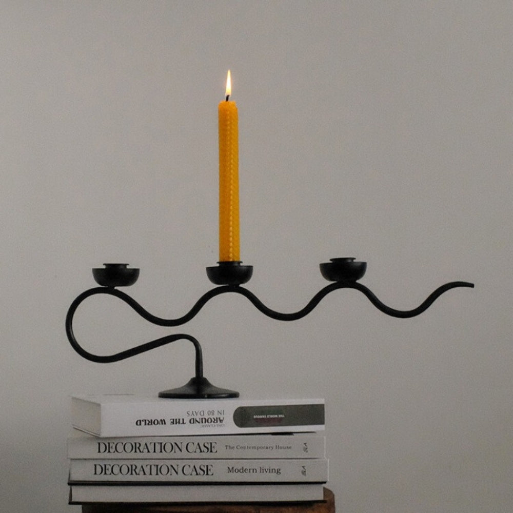 Black three-headed twisted iron candle holder with a yellow candle lit on top.