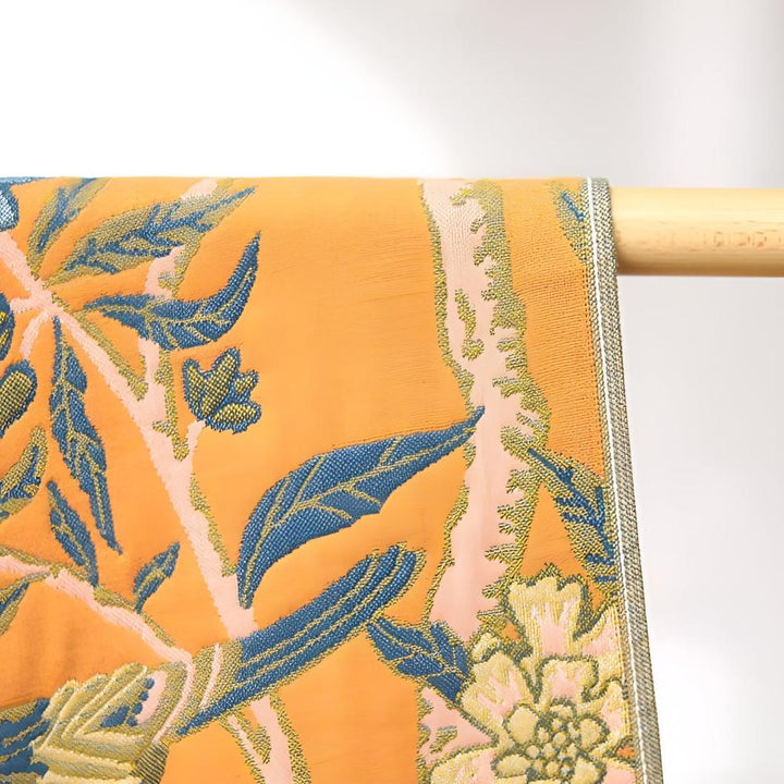 Orange cotton bath towel with a blue floral and leaf pattern, hanging on a wooden rod.