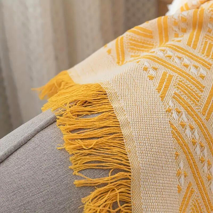 Yellow and white geometric patterned throw blanket with fringe detail draped over a grey sofa.