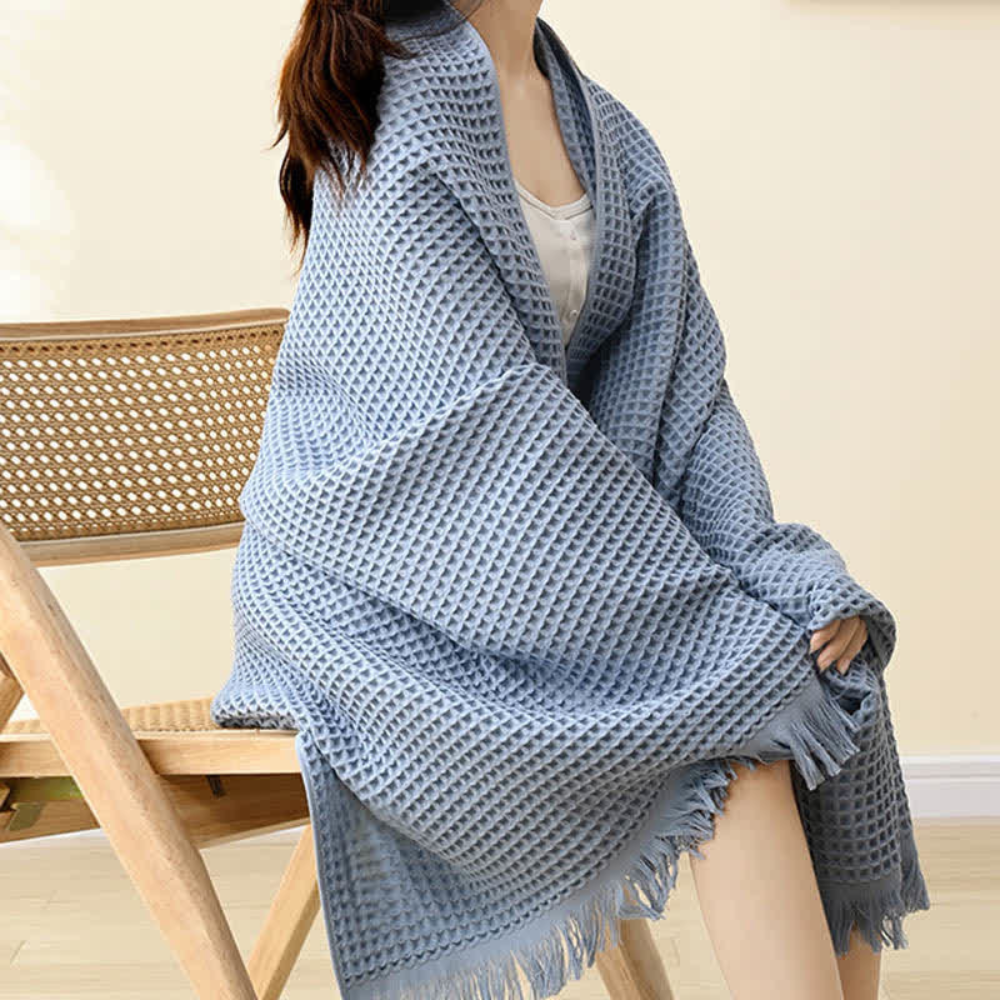 Woman wearing a light blue waffle-weave cotton towel like a shawl, sitting on a wooden chair.