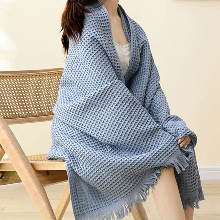 Woman wearing a light blue waffle-weave cotton towel like a shawl, sitting on a wooden chair.