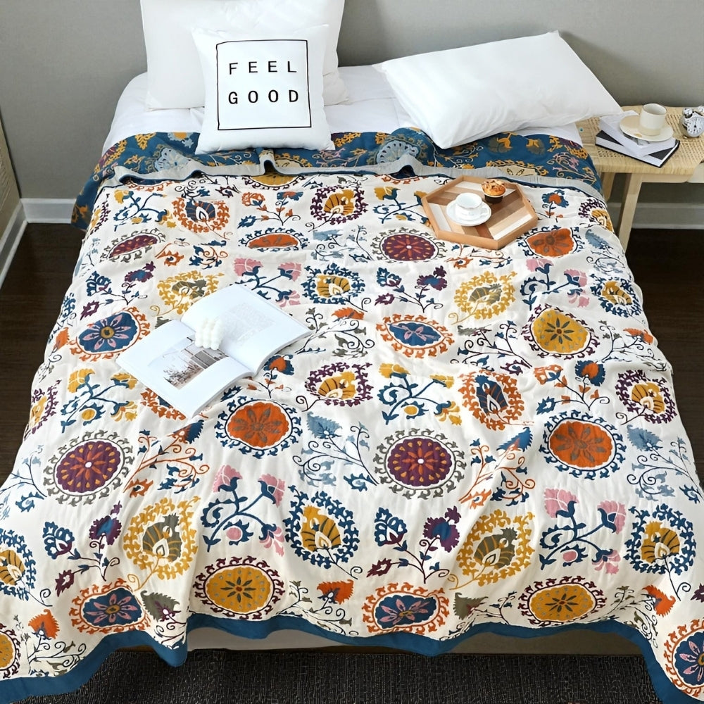 A bed with a colorful floral gauze coverlet, white pillows, and an open book.