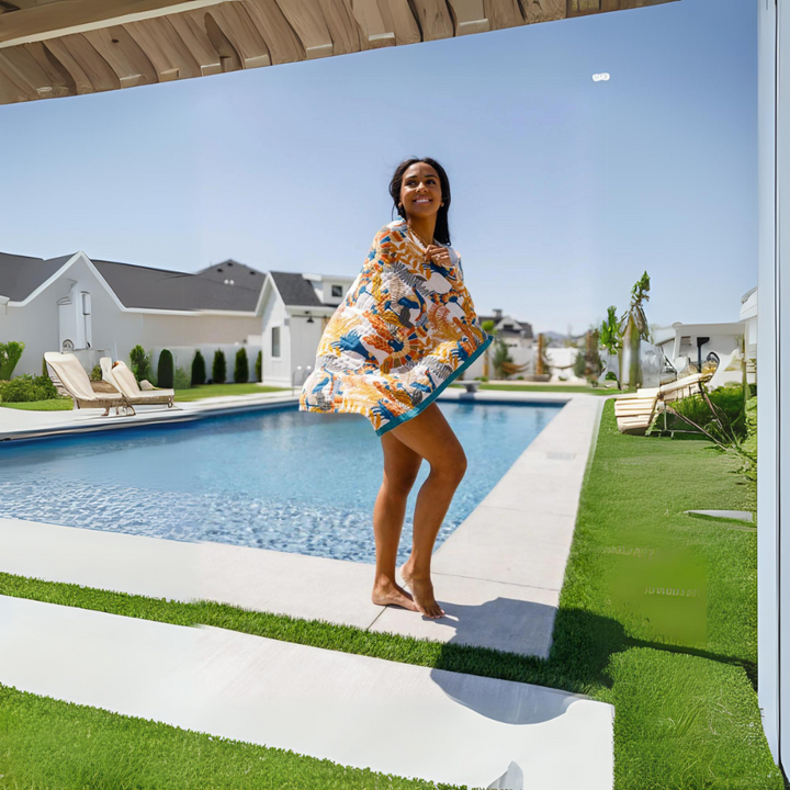 Woman wrapped in a reversible cotton beach towel with a floral and bird print, standing by a swimming pool.